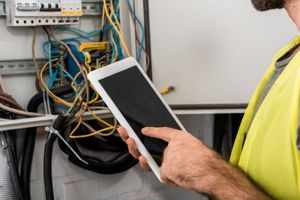 A technician inspecting an industrial electrical panel with a tablet.